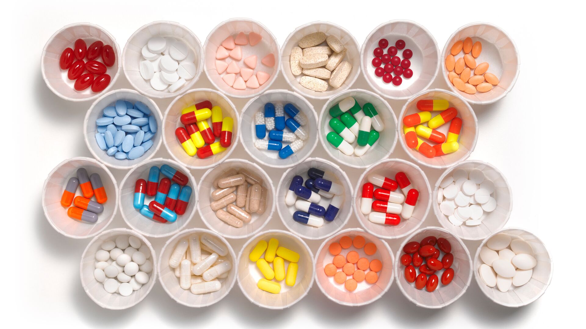 Dixie cups lined up in rows appear to contain a variety of prescription medication visible from a top down view against a white background.