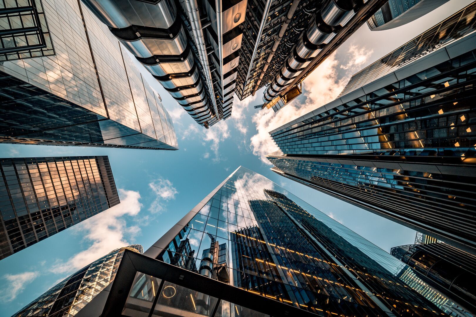 An upward-perspective from a street level between tall, modern buildings beneath a blue sky.