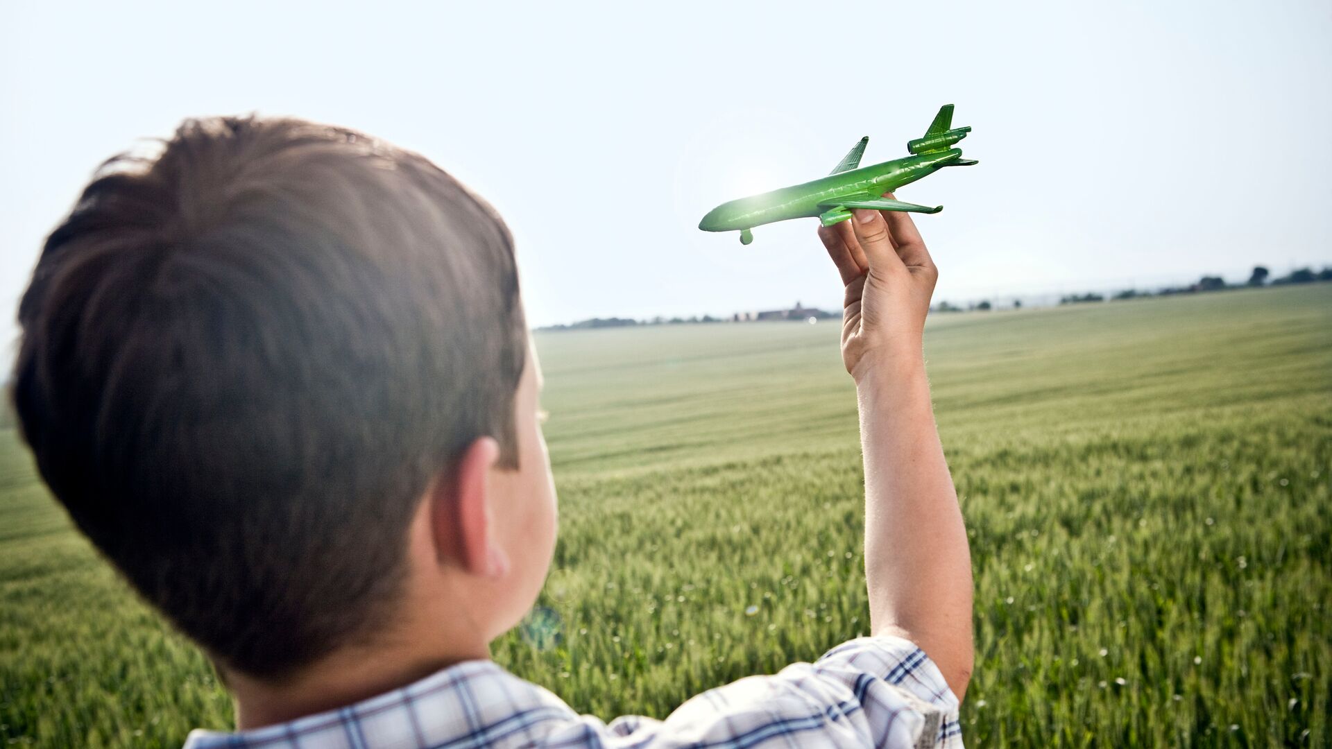 Boy playing with green paper plane in green field. The boy is flying the plane through the air. Sustainable air travel concept for a piece on sustainable aviation fuel and the aviation industries ESG & Net Zero commitments.