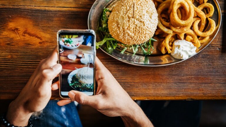 A person photographing their cheeseburger delux with onion rings. For Cowen's latest Podcast Series, Restaurant Rendezvous