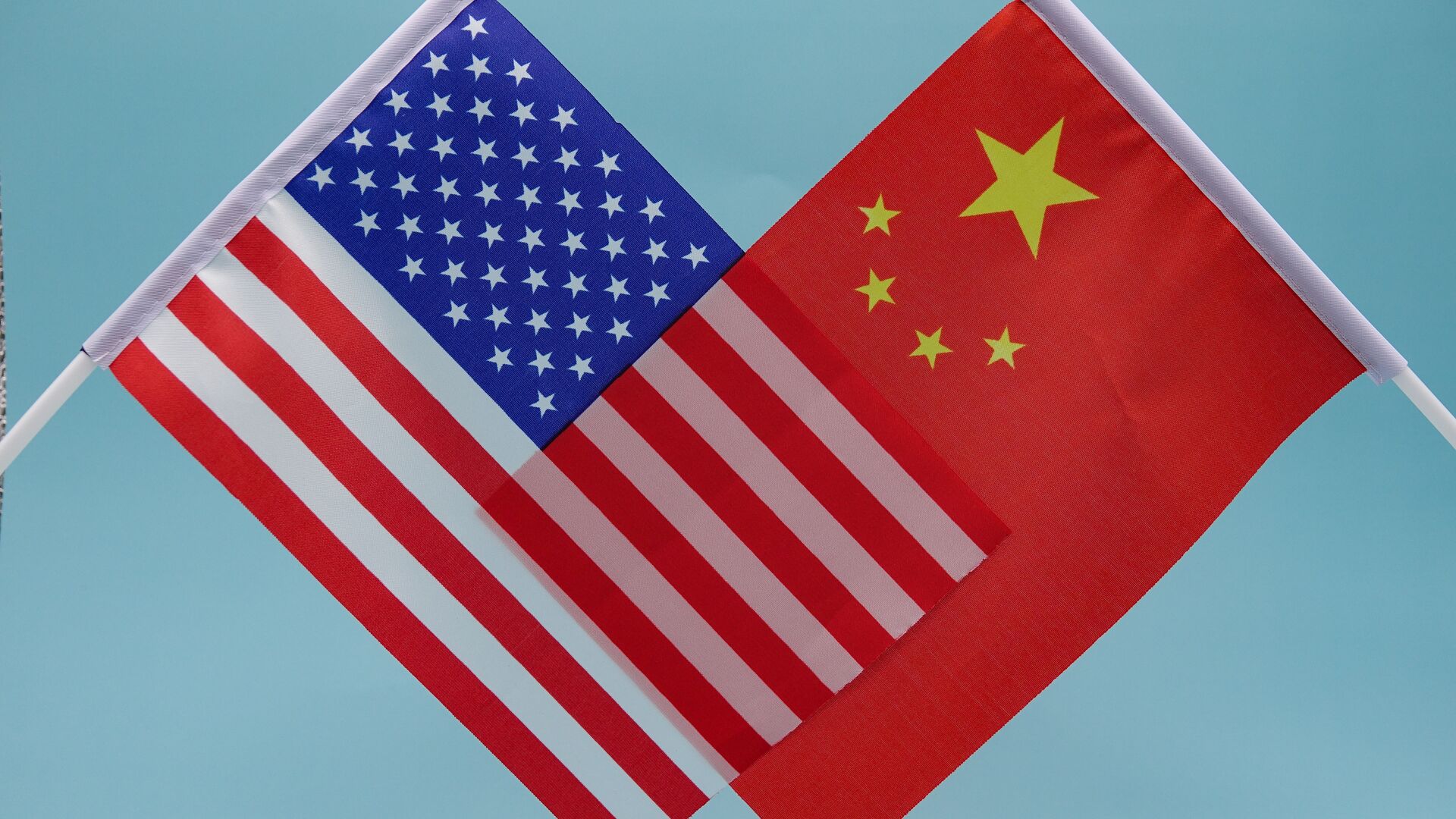 The U.S and Peoples Republic of China flags held one in front of the other against a blue backdrop, blending their colors while showing opposing sides at odds. Representative of U.S China Relations simmering.