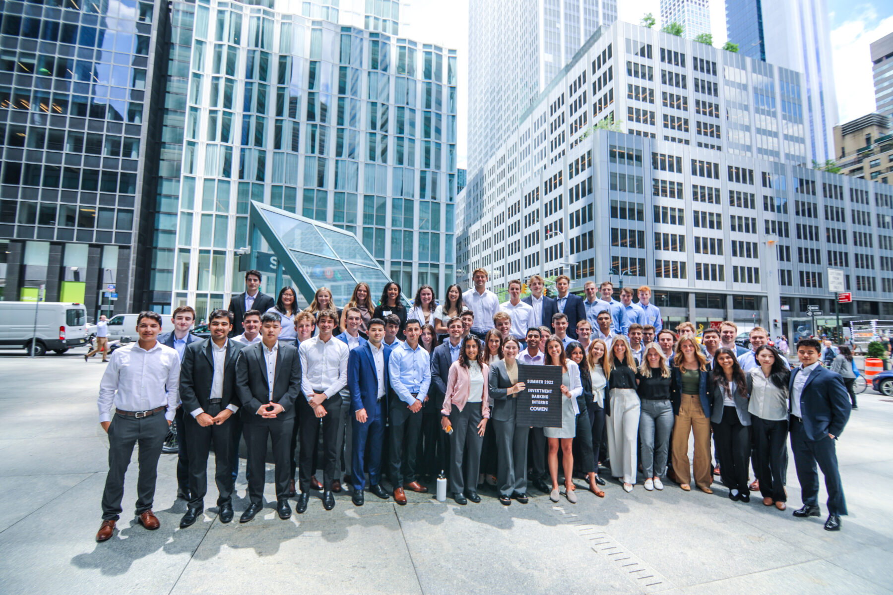 Large group of employees posing together for a photo outside with skyscrapers in the background
