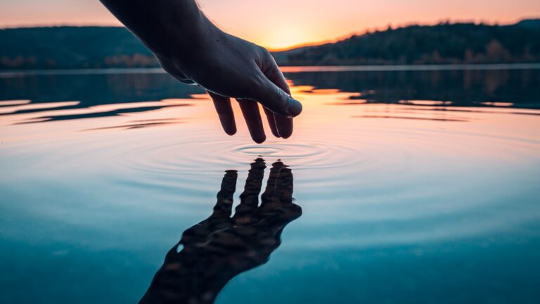Finger touching a placid lake with the sun in the horizon, it is our natural water supply, representing the need for water muni budgets to be supported in a world that isn't