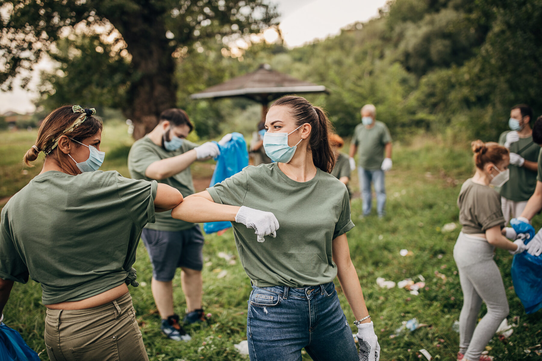 Group of people, cleaning together in public park, saving the environment together, all of them are wearing surgical masks due to coronavirus.