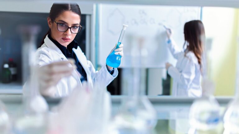 Health Care Innovation in Research and Development depicted by two lab scientist conducting research in a lab. Blue and white color scheme with two female Scientists.
