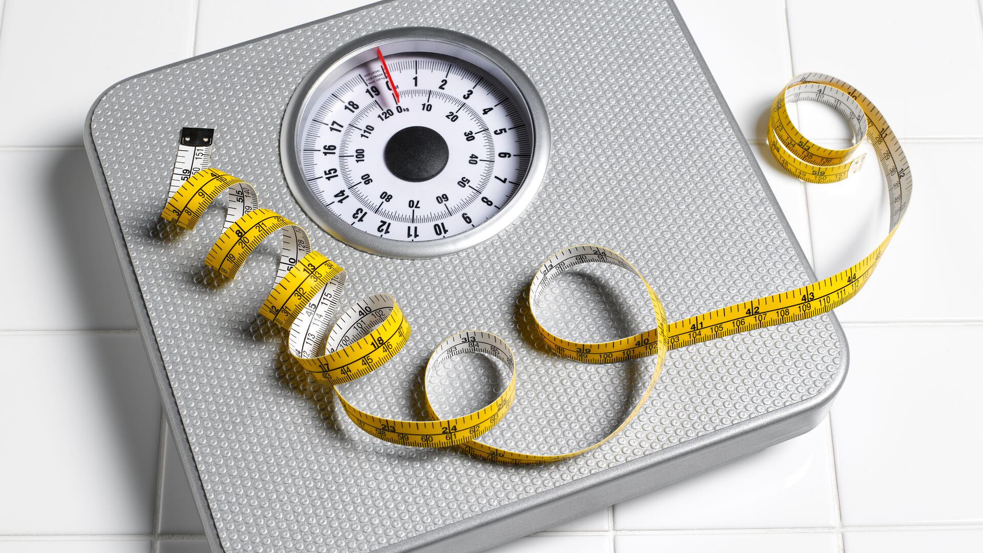 Representing research into Obesity drug market is a scale and an exhausted tape measure resting on the scale. Against a white background and the scale is old fashioned.