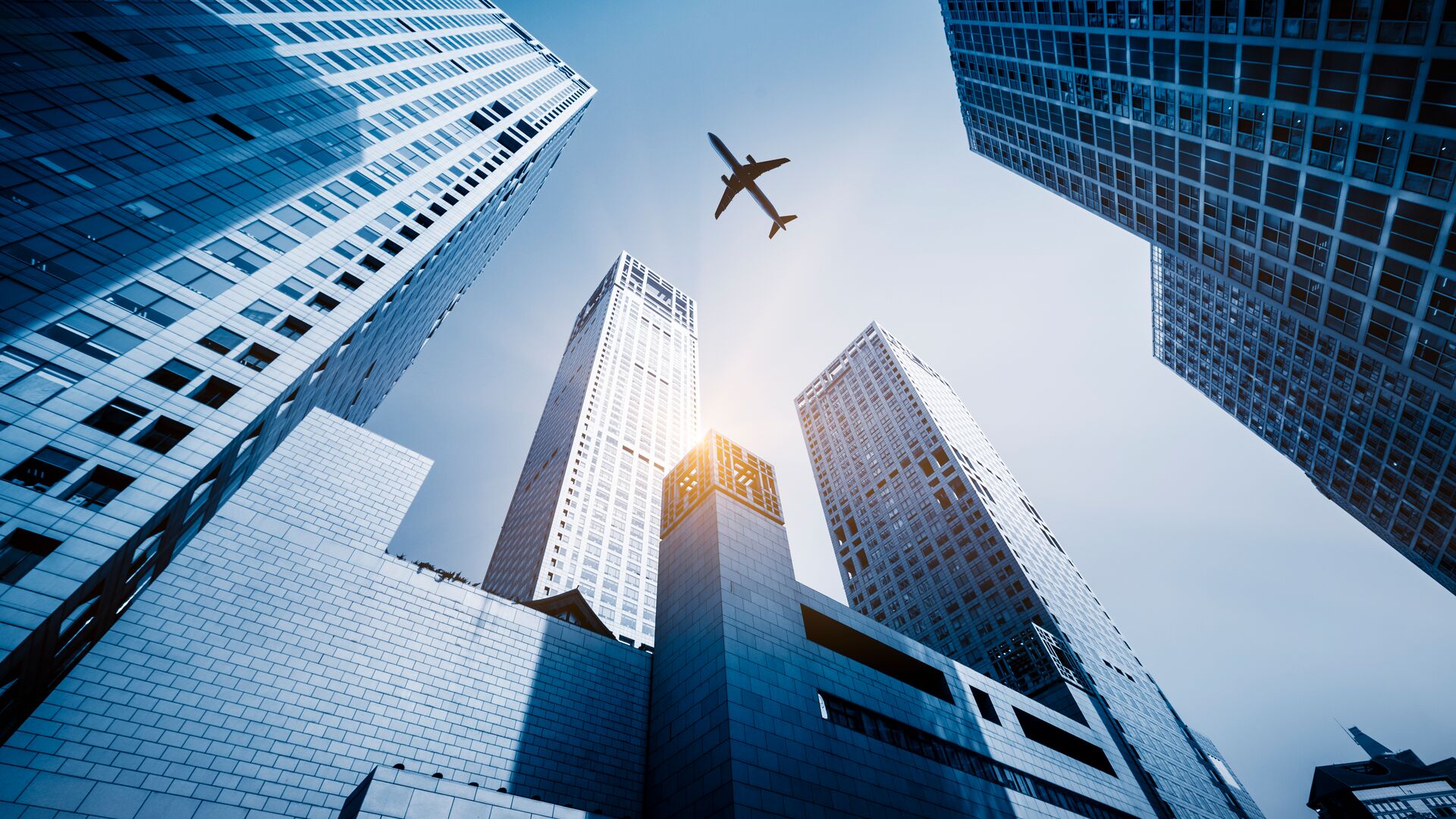 Looking up from the ground on a plane flying over office building in a financial district representing a report on the aftermarket for aerospace and airlines,.