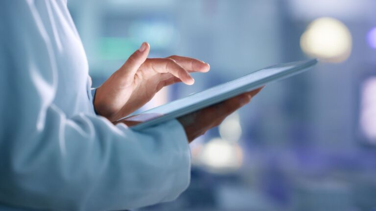 Shot of a health care professional in a doctors coat using a digital tablet to administer care, representing our recent podcast on telehealth.