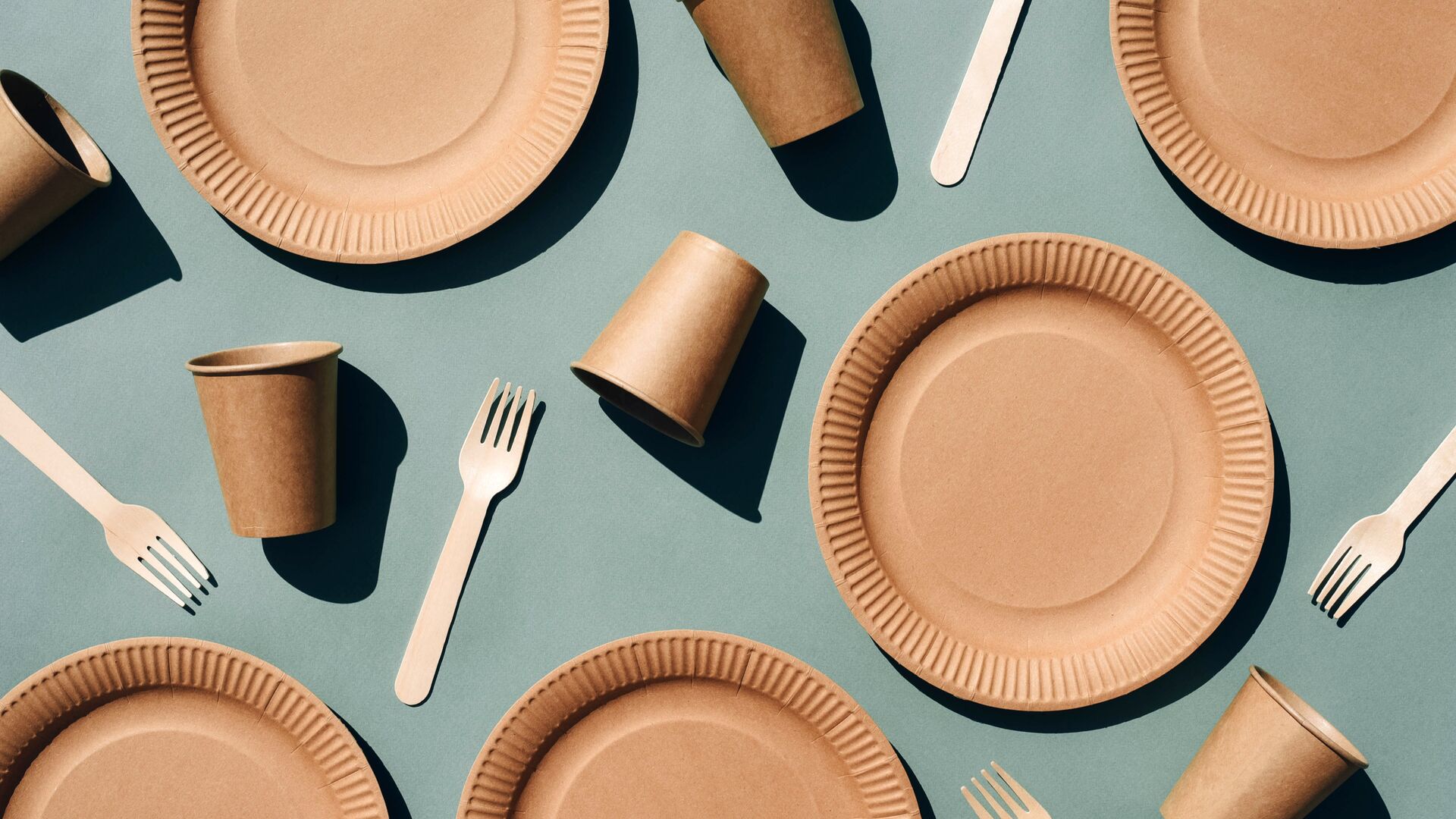 A shot looking down on Biodegradable utensils, plates, and cups against a blue-green background representing our recent podcast with Chipotle on their ESG priorities.