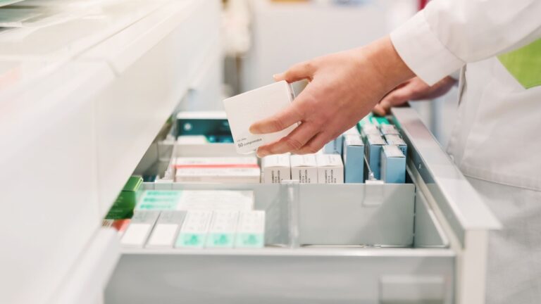 Pharmacist pulls out medicine from pull out white drawer.