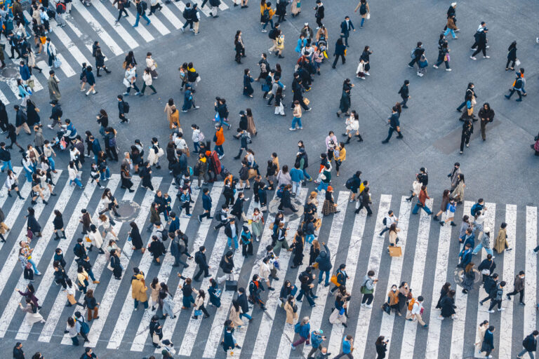 An overhead view of a large group of people crossing large intersections in a city setting.
