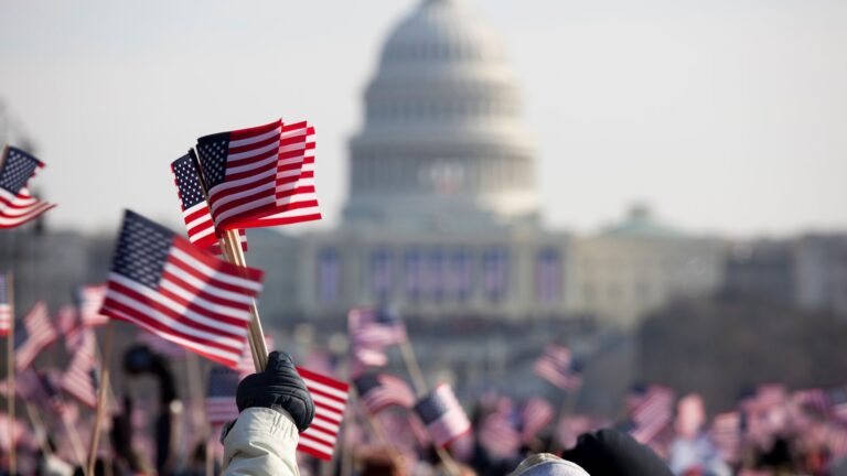 Small American flags waving in the hands of citizens celebrating an election in front of the white house during the day.